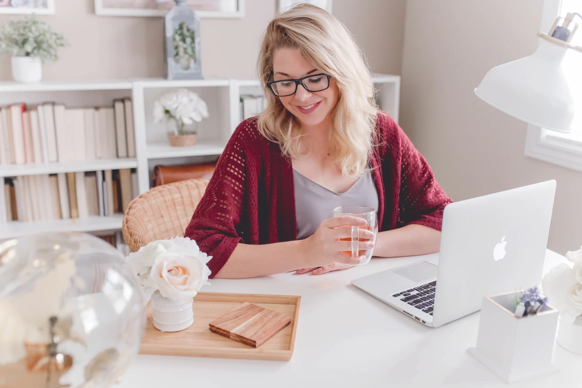 A candidate with glasses smiling at her desk, with books on the shelves behind her.