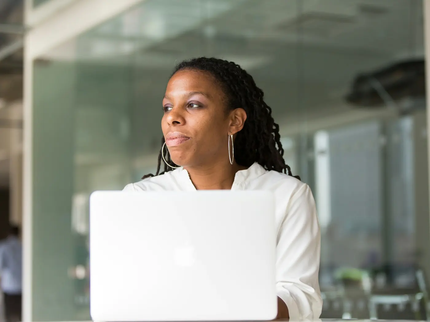 Someone sitting at a laptop, looking away from the screen and thinking.
