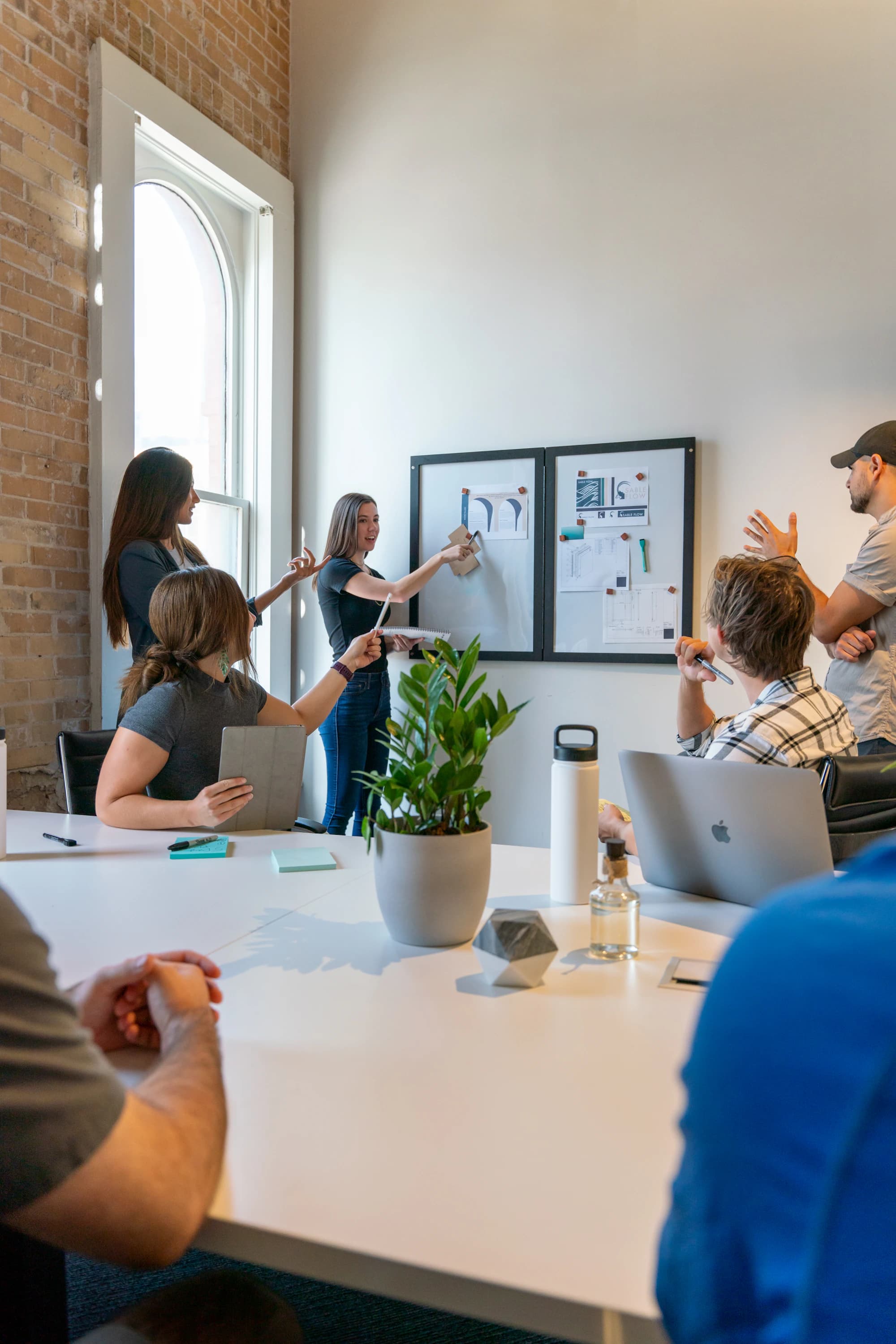A product team standing around a whiteboard covered in notes, with a plant on the table.