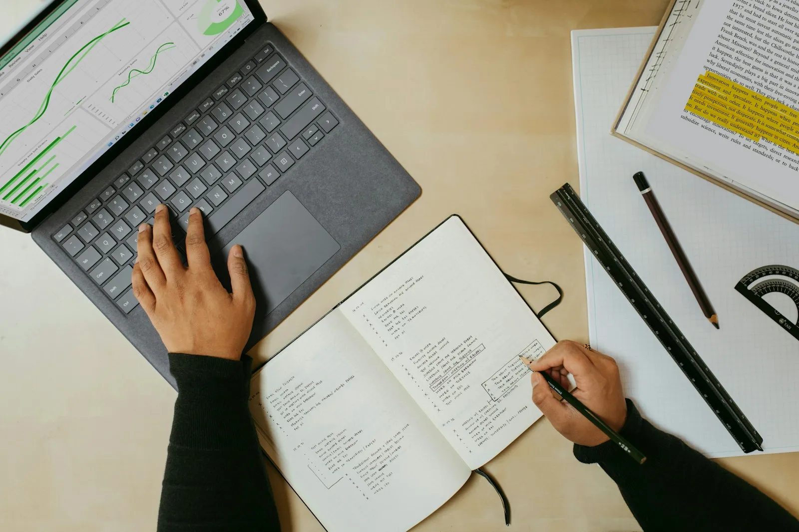 A laptop showing charts next to an open notebook full of handwritten research notes.